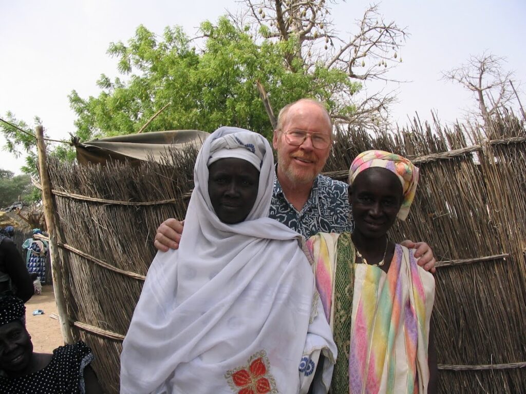 A man stands between two women in traditional attire outdoors.