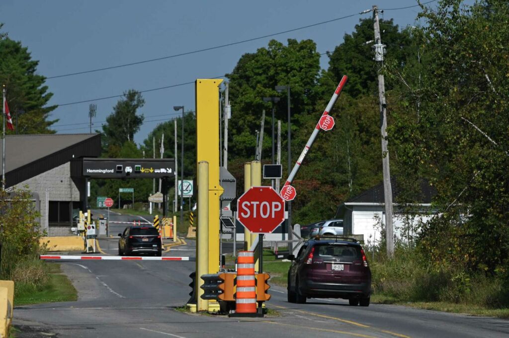 A car waits at a railroad crossing with lowered gates and a stop sign.