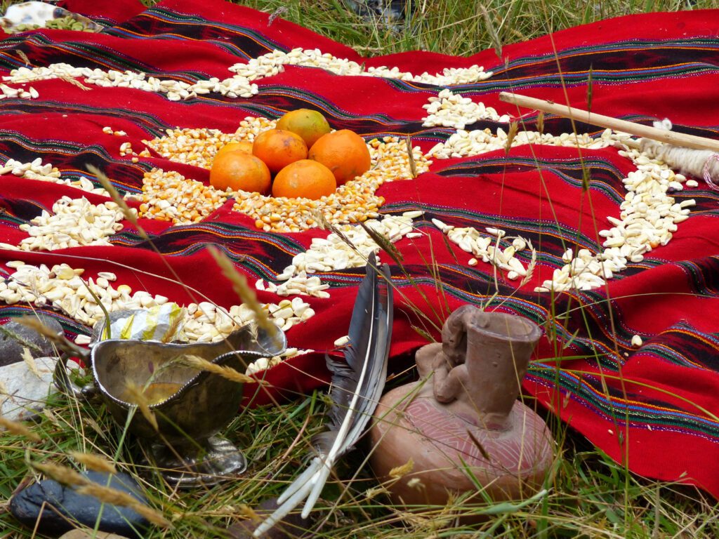 Traditional arrangement with fruits, grains, feathers, and pottery on red cloth.
