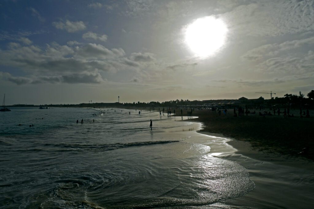 Sunset over a calm beach with gentle waves and people.