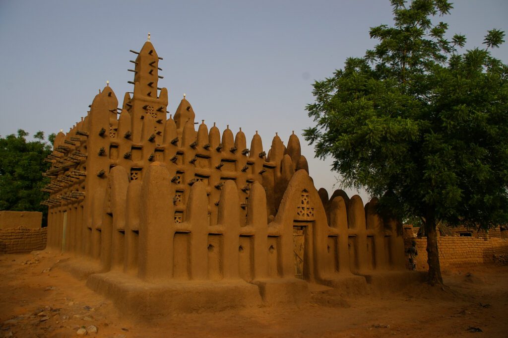Traditional mud-brick mosque with intricate spires under a clear sky.