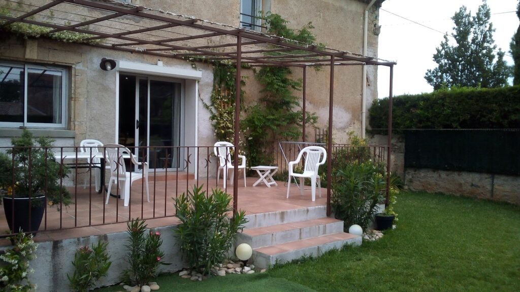 Cozy patio with white chairs and greenery beside a house.