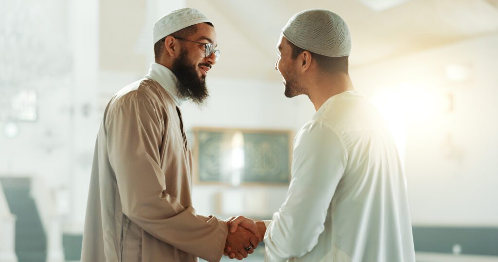 Two men in traditional Muslim attire shaking hands warmly.