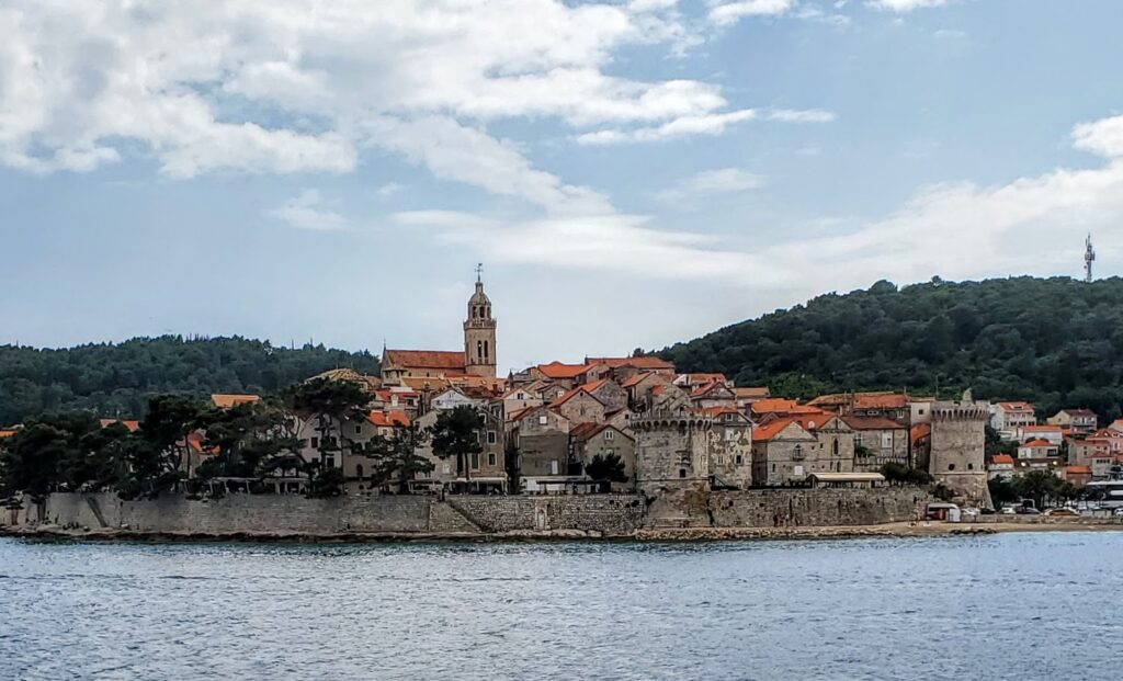 Coastal town with historic buildings and a church tower under a cloudy sky.