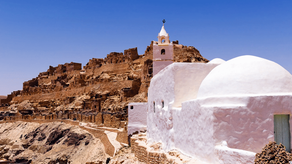 Whitewashed buildings and ruins on a rocky hill under a clear sky.
