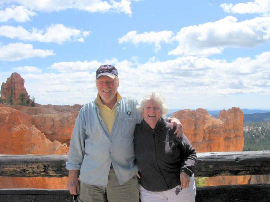 An elderly couple posing together outdoors with a scenic canyon backdrop.