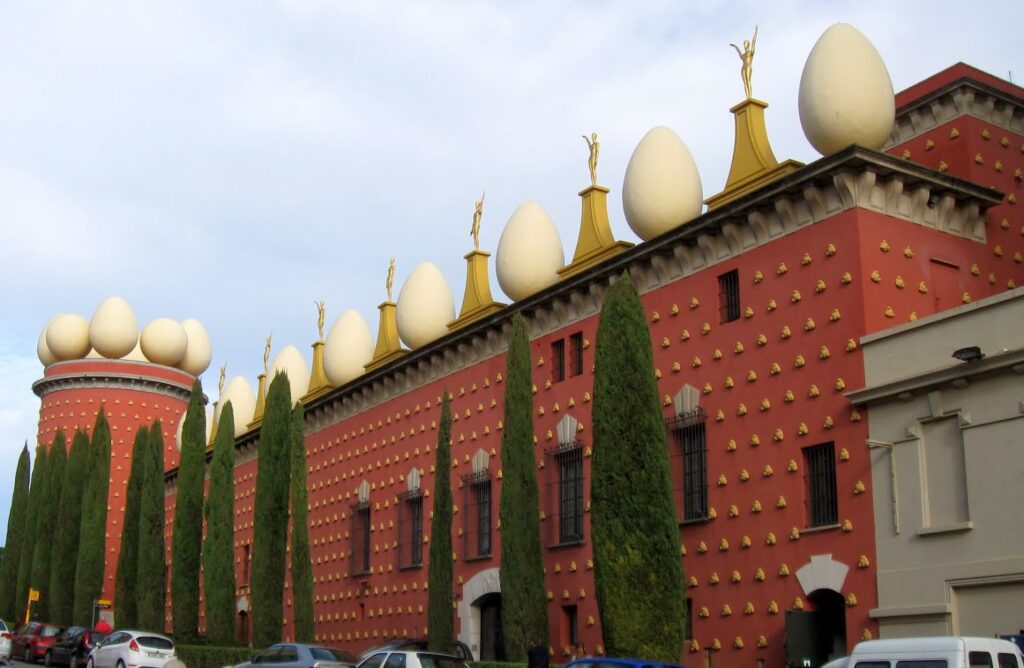 Surrealist museum facade with large egg sculptures on the roof against a cloudy sky.
