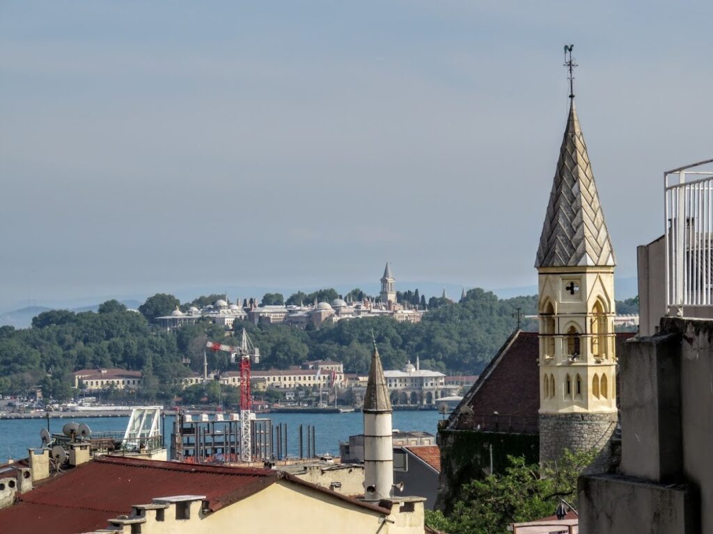 View of a cityscape with a church tower and distant buildings under a clear sky.
