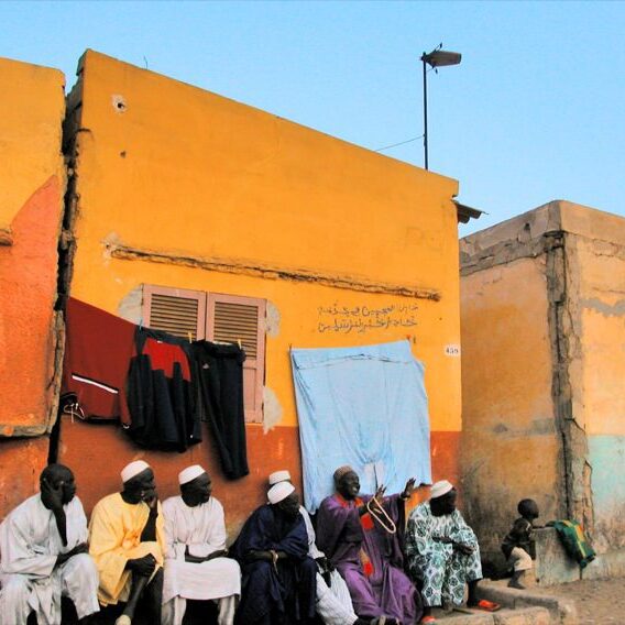 People gather outside vibrant orange buildings under a clear sky.