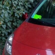 Close-up of a red car's front with a green sticker on the windshield.