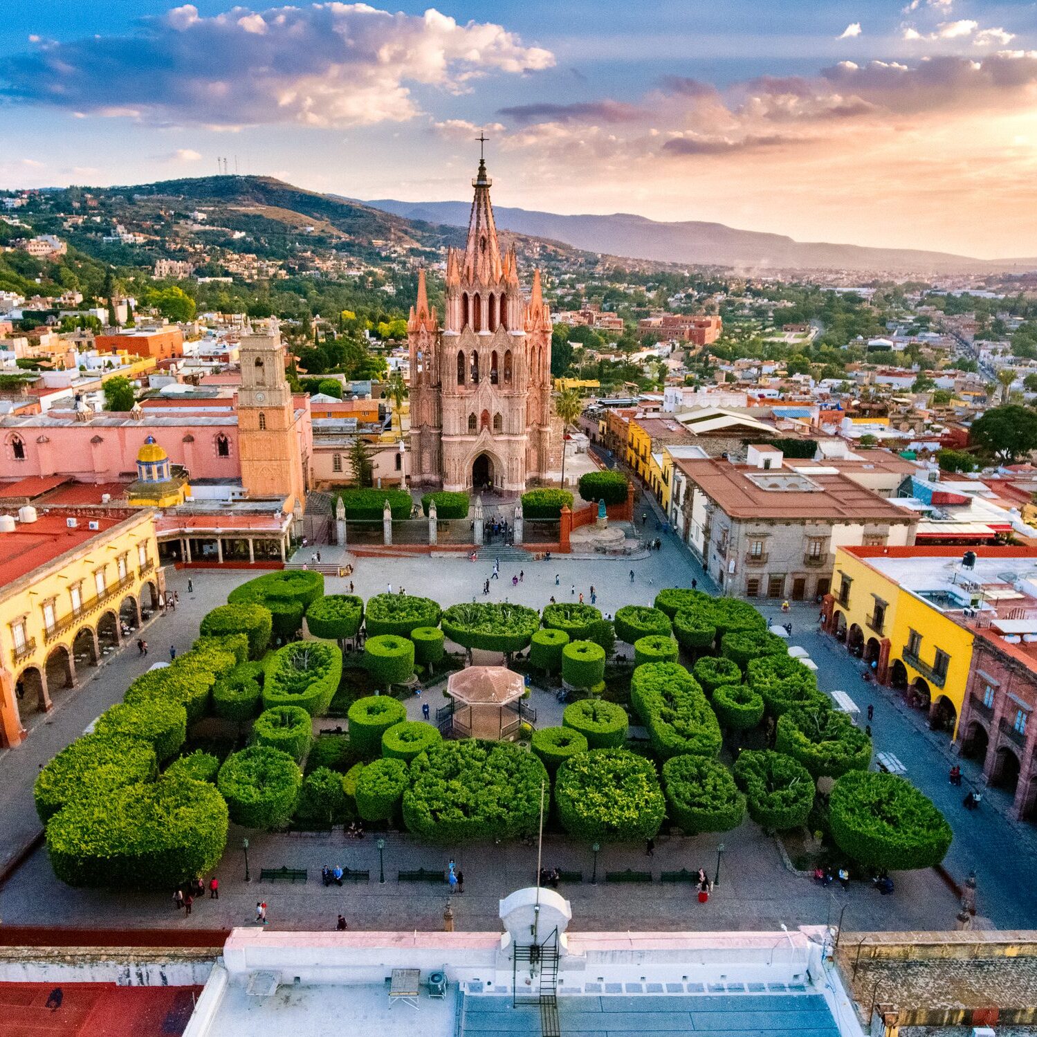 A vibrant city square with a historic church and lush greenery at sunset.
