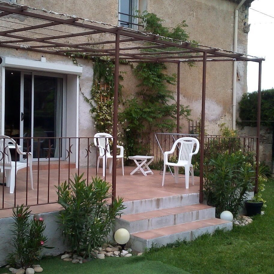 Cozy patio with white chairs and greenery beside a house.