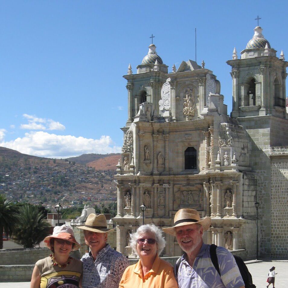 Four tourists posing in front of a historic cathedral with blue sky.