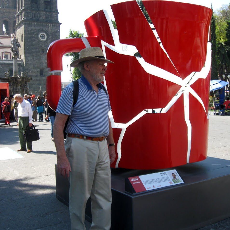 Man standing next to a large cracked red coffee cup sculpture.