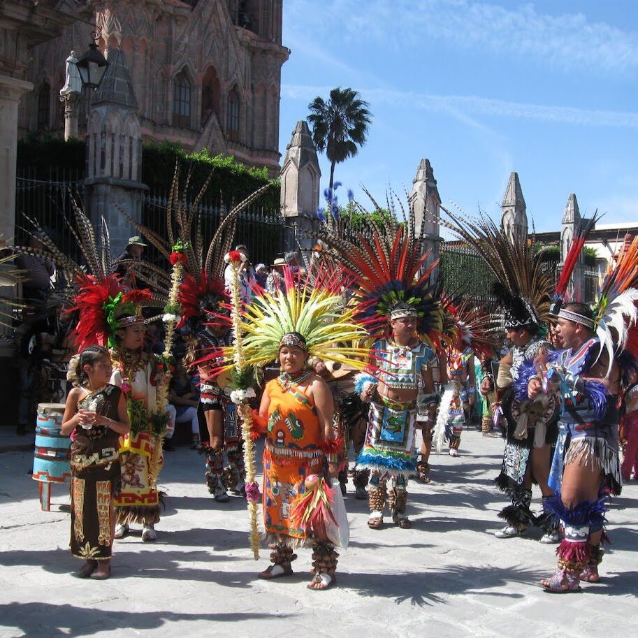 Group in colorful traditional Aztec attire performing outdoors.