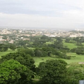 Panoramic view of a green landscape with scattered buildings in the distance.